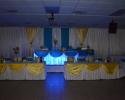 White, yellow and blue drapery covering the reception walls and tables. Bride and groom table is lit up with special lights. 