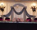Black table cloth and chair covers with accents of magenta enhanced by metallic drapes and a line of lights.