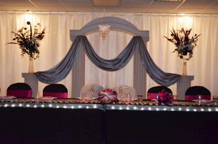 Black table cloth and chair covers with accents of magenta enhanced by metallic drapes and a line of lights.