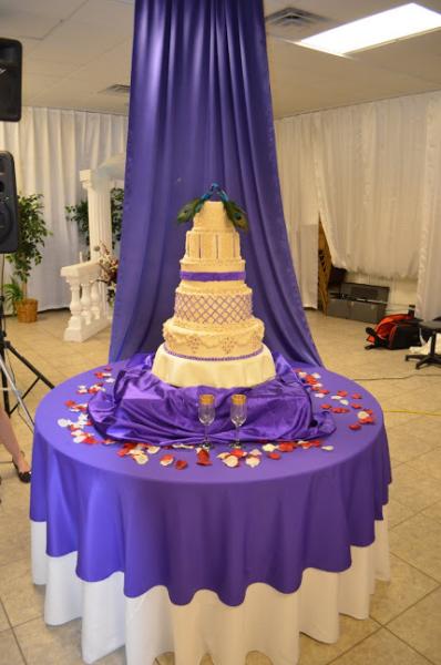 This gorgeous wedding cake table features beautiful purple and white accents to match the cake. The drapery behind the cake makes it stand out even more!