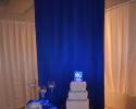 Round lit up cake table with blue and white drapery. 