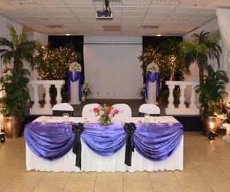 A gorgeous wedding with purple, black and white. This white head table looks stunning with the purple drapery and black accents.