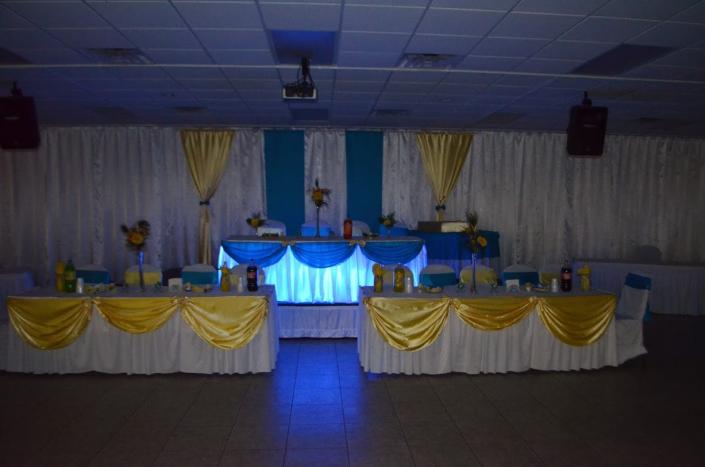 White, yellow and blue drapery covering the reception walls and tables. Bride and groom table is lit up with special lights. 